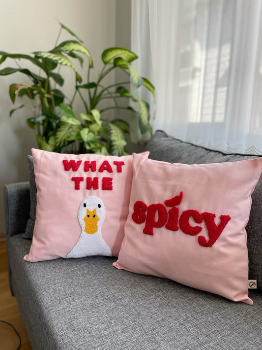 Two pink pillows with text and a duck illustration on a gray couch. Soft chaos duo tufted cotton cushion covers with text and character design.