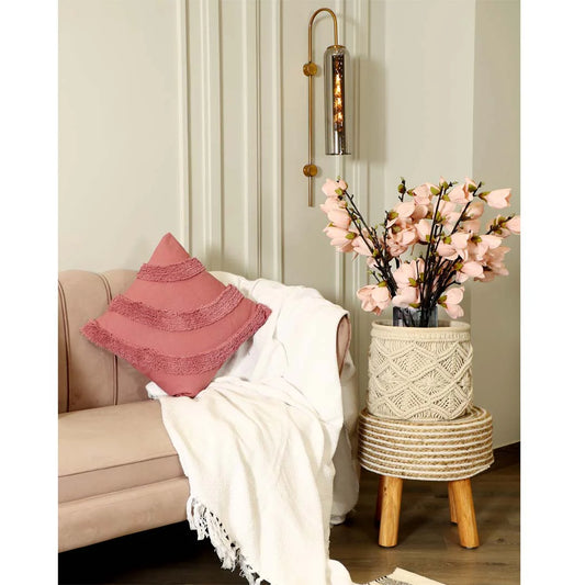 Living room with a beige sofa, pink pillow, white blanket, and decorative plant on a wooden stool.