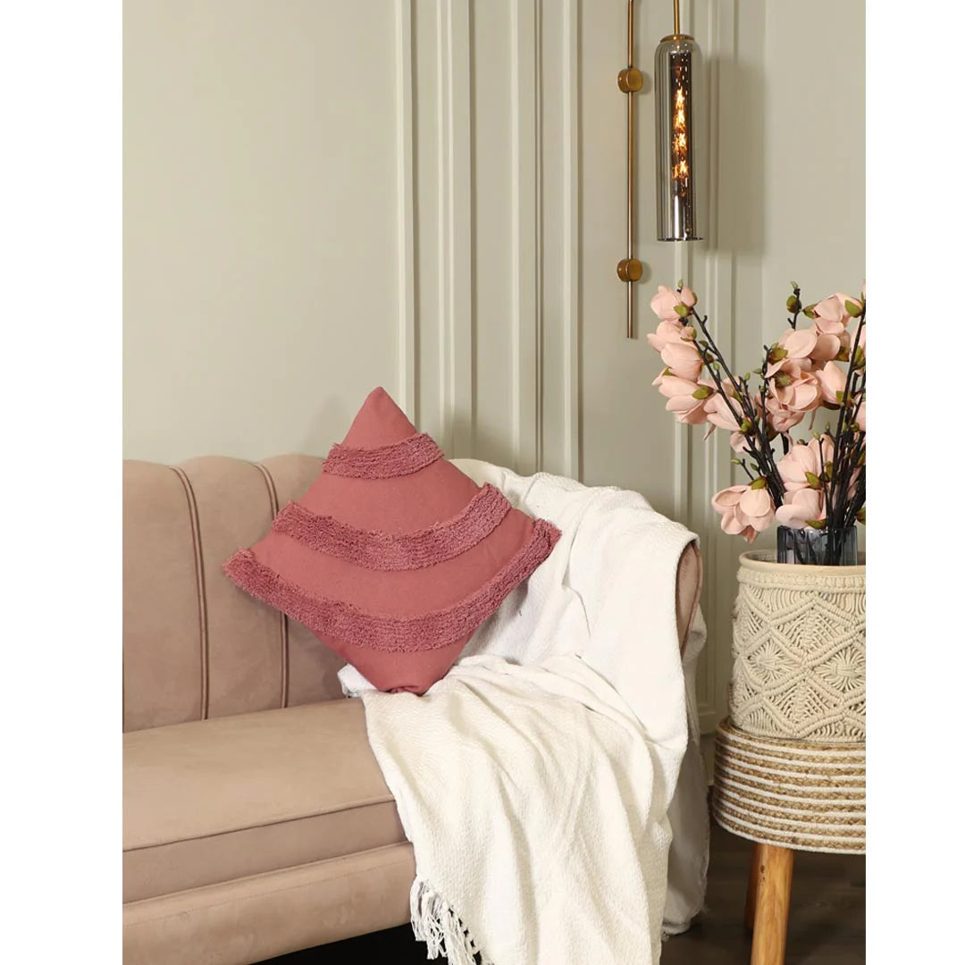 Beige sofa with a pink pillow and white blanket, next to a small table with flowers.