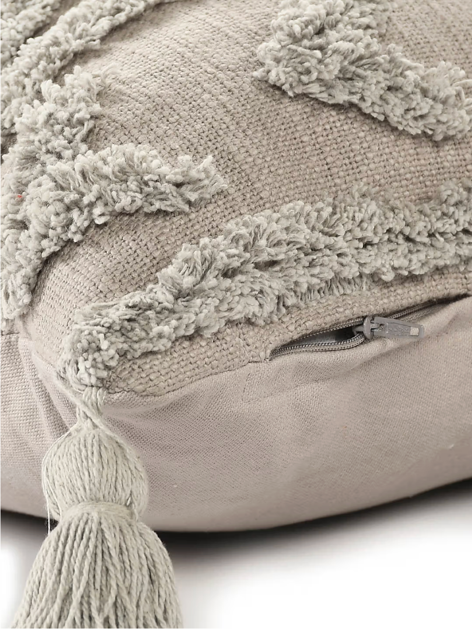 Beige pillow with textured surface and tassels on a light background