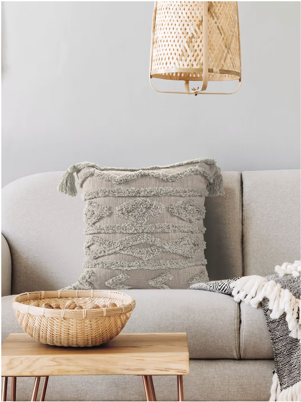 Gray textured pillow on a beige sofa with a wooden coffee table and woven lamp in a living room setting.