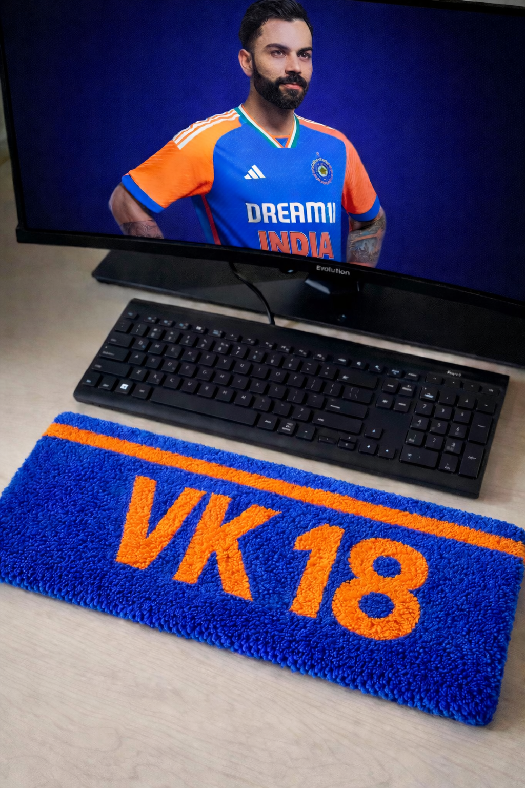 Virat Kohli inspired VK 18 keyboard rug in India blue and orange on a modern desk setup by Cozy Bear
Computer setup with a monitor displaying a person in an orange and blue sports jersey, a keyboard, and a blue and orange mat with 'VK 18' on a desk.