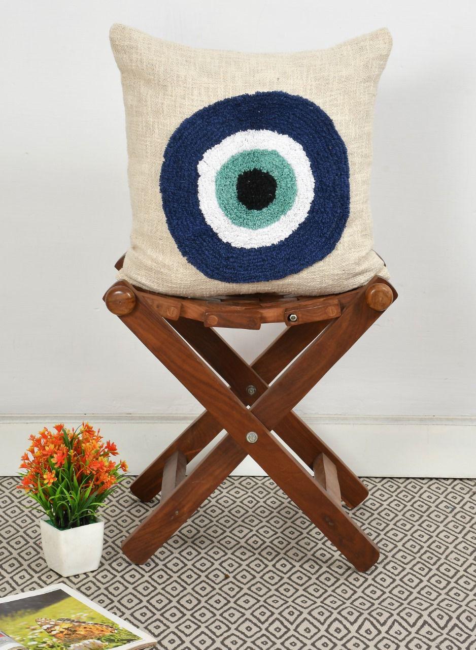 Blue Evil eye tufted cotton cushion cover with concentric circle design.
Decorative pillow with a circular pattern on a wooden stool against a white wall.
